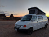 White pop-top camper van for your next RV rental adventure, parked at sunset amidst desert rock formations.