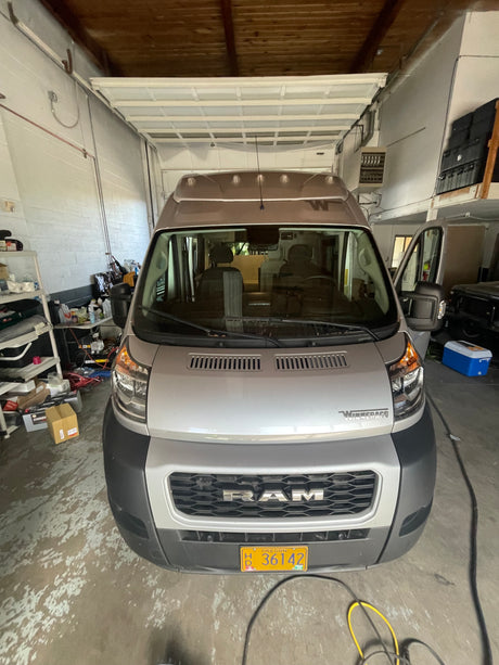 A silver Winnebago camper van (RV rental) parked in a garage. Its driver's side door is open, showing the interior.