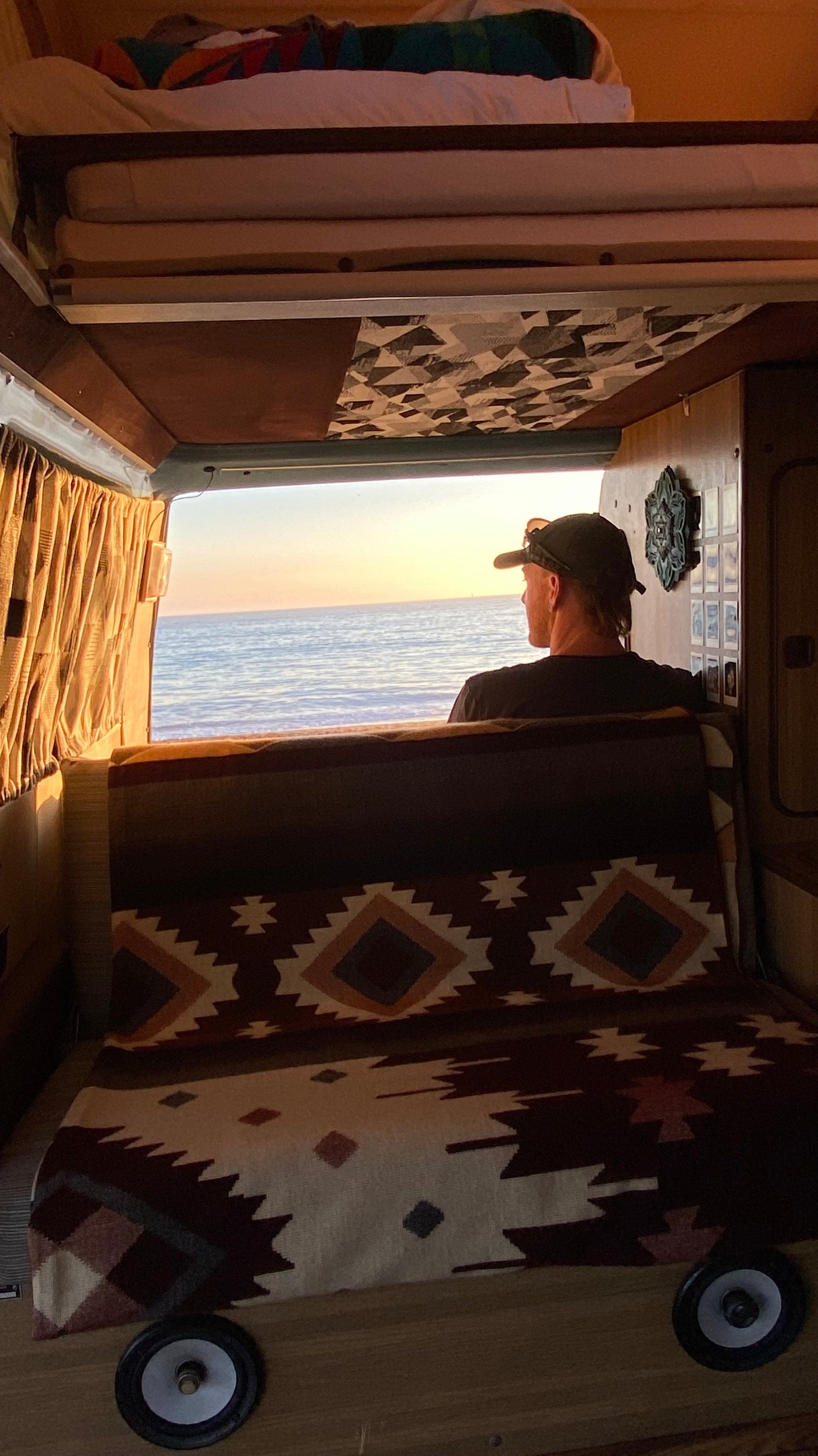 RV rental sunset: Person watching the ocean from a cozy camper van interior.