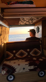 RV rental sunset: Person watching the ocean from a cozy camper van interior.