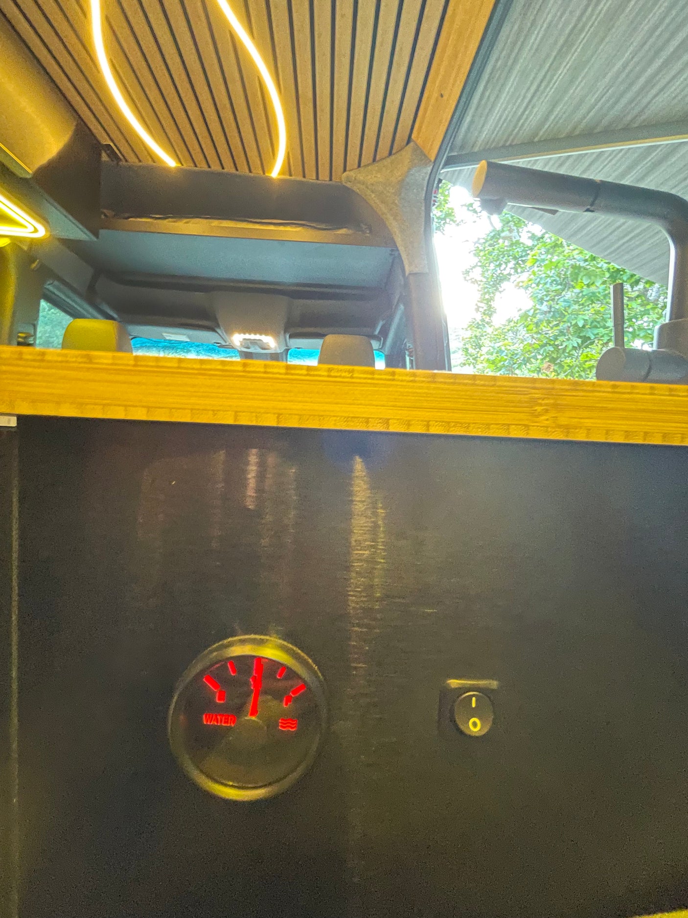 Inside a custom **rv rental**: wooden ceiling with LED lights & a water level gauge on a control panel with a power switch.