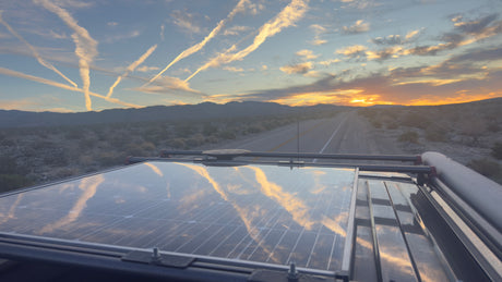 Stunning RV rental view: Desert landscape at sunset with sky contrails mirrored on the vehicle's solar panel.