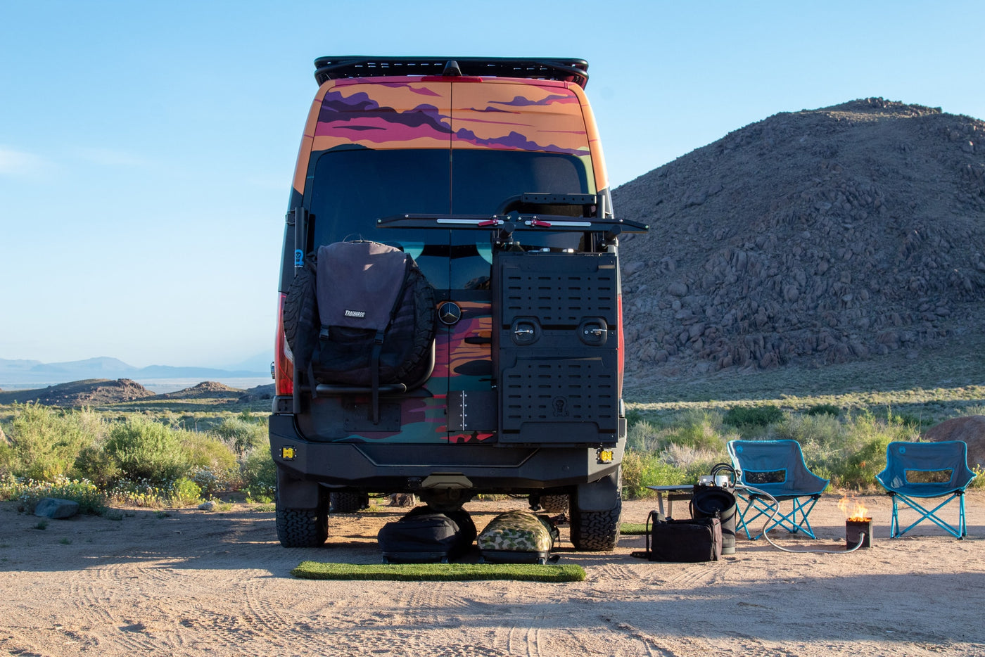  with chairs and a cozy fire pit behind the colorful van.|Colorful custom RV rental parked for camping with mountain views — photo 8