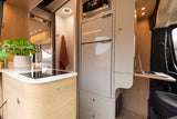 Modern RV rental interior: compact kitchen with stove, fridge, microwave, bathroom, and workspace with laptop.
