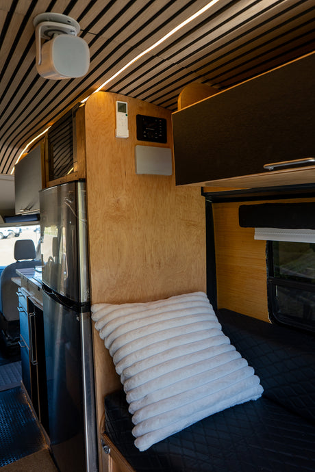 Cozy RV rental interior with slatted wooden ceiling, LED lights, fridge, tech controls, and plush seating for van life comfort.