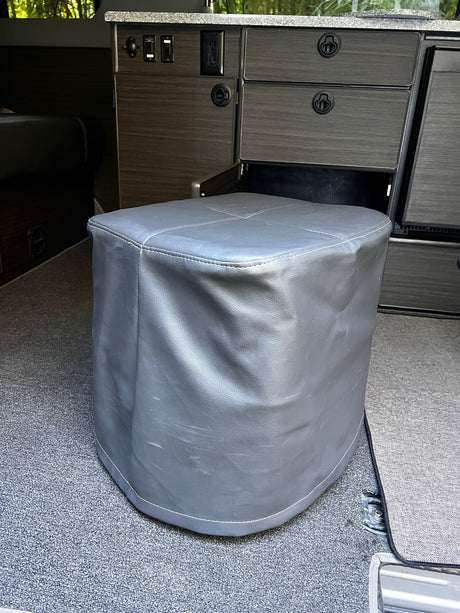 Grey faux leather ottoman in an RV rental, surrounded by custom dark wood cabinetry and carpet.