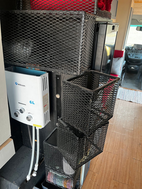 Compact rv rental interior featuring a Wilson 6L water heater, wall-mounted mesh storage, and a glimpse of the driver's cabin.