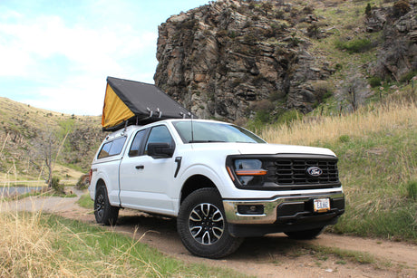 A white Ford F-150 truck with a rooftop tent on its camper. Ideal for an RV rental or off-road adventure through rocky terrain.