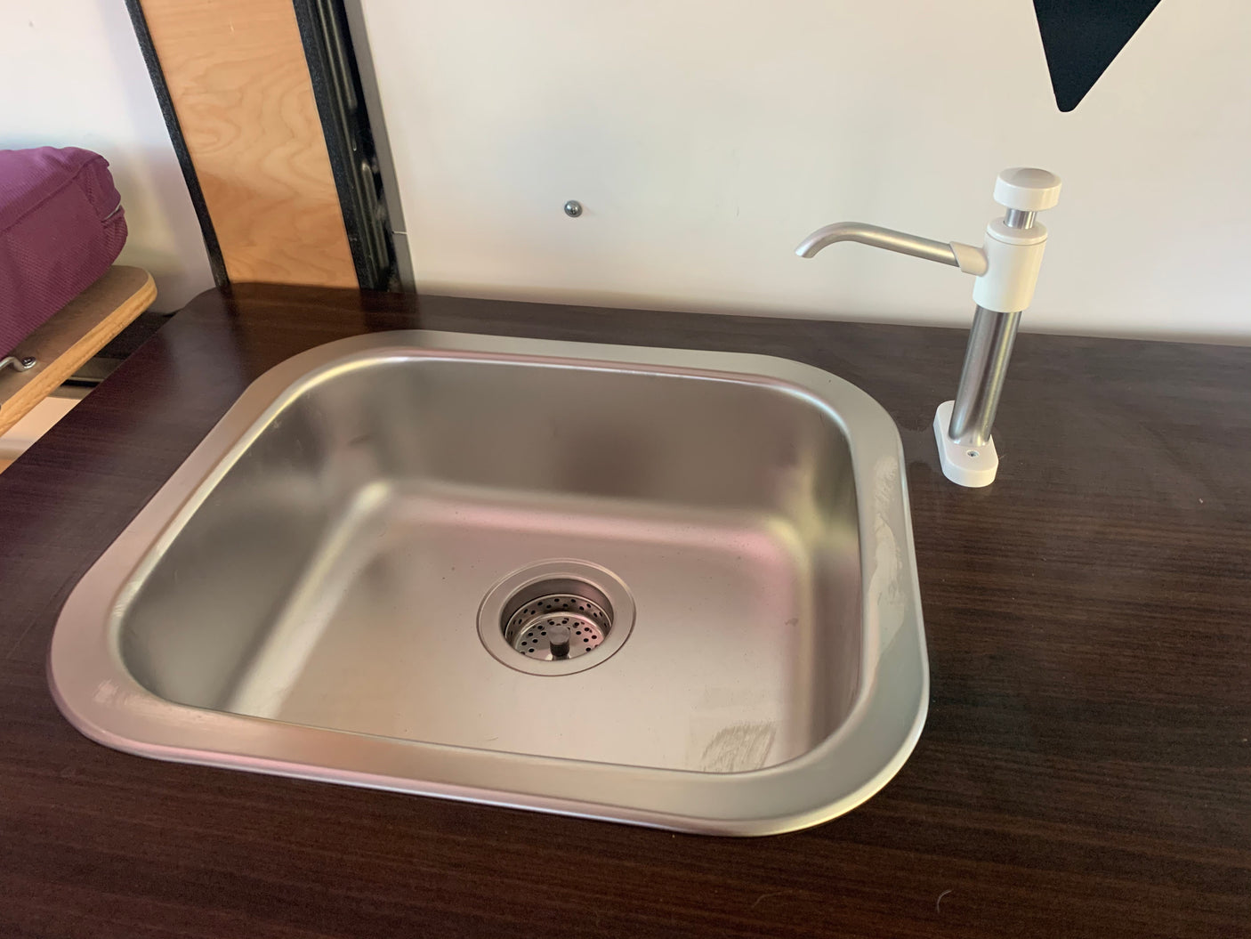 This RV rental features a compact, clean stainless steel sink with a white faucet on a dark wood counter.