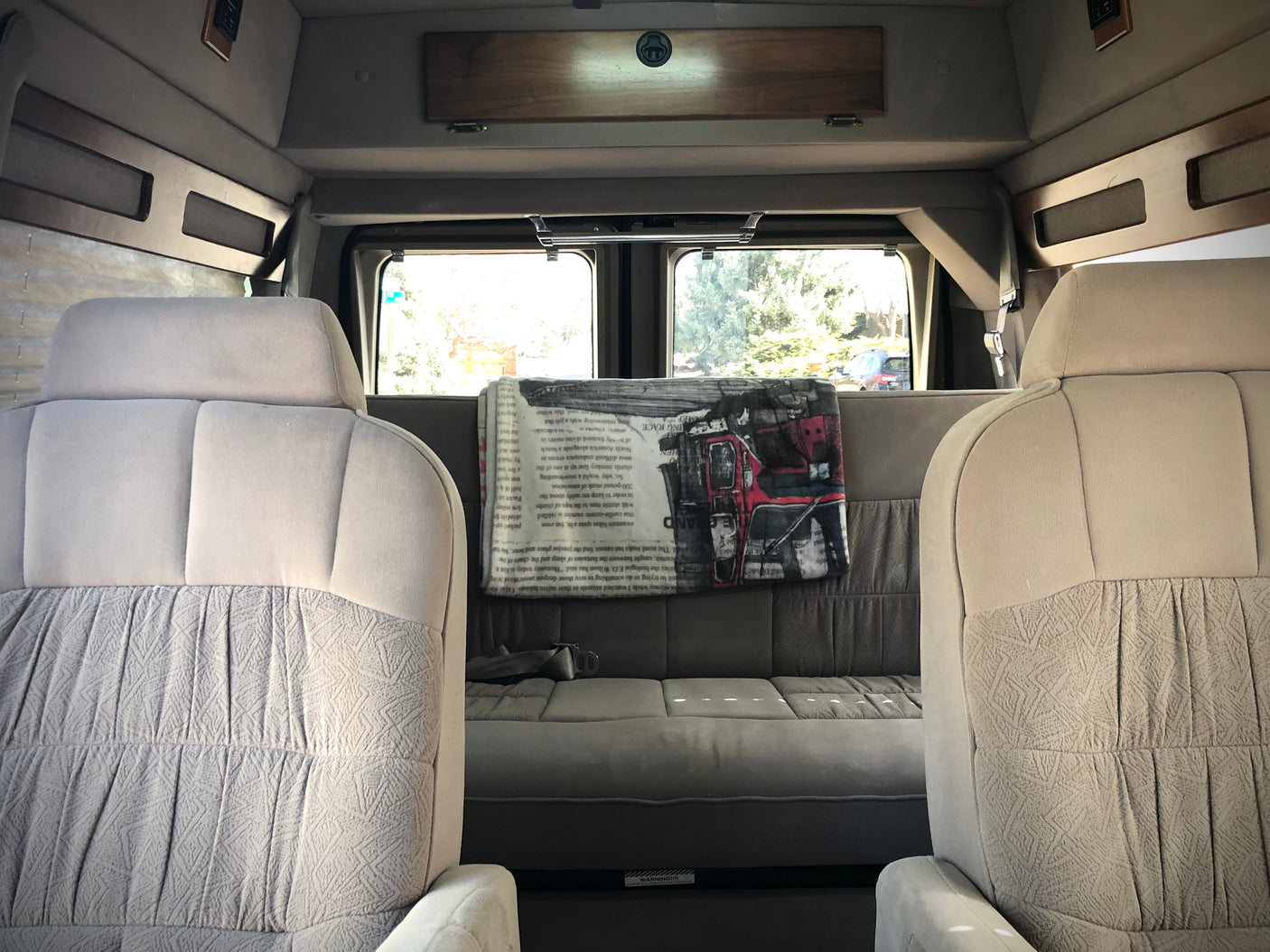 Comfortable RV rental van interior with light-colored front seats, a grey rear sofa, and large windows.
