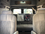 Comfortable RV rental van interior with light-colored front seats, a grey rear sofa, and large windows.