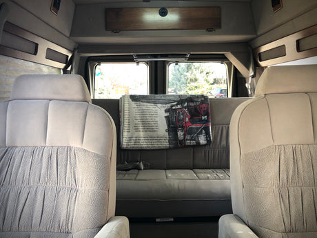Comfortable RV rental van interior with light-colored front seats, a grey rear sofa, and large windows.