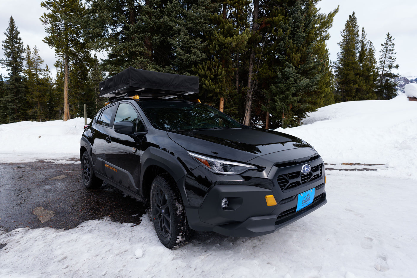 Black Subaru Crosstrek with a rooftop tent for rv rental, parked in a snowy forest. Ideal for winter adventure.