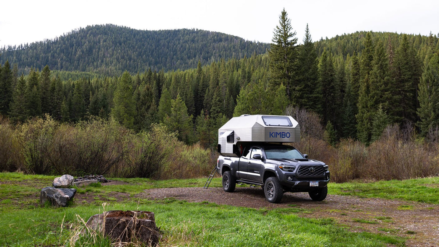 Explore nature with an RV rental: a Kimbo truck camper on a pickup truck parked in a lush, green forest campsite.