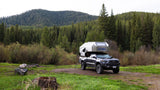 Explore nature with an RV rental: a Kimbo truck camper on a pickup truck parked in a lush, green forest campsite.