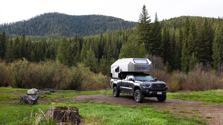 Explore nature with an RV rental: a Kimbo truck camper on a pickup truck parked in a lush, green forest campsite.