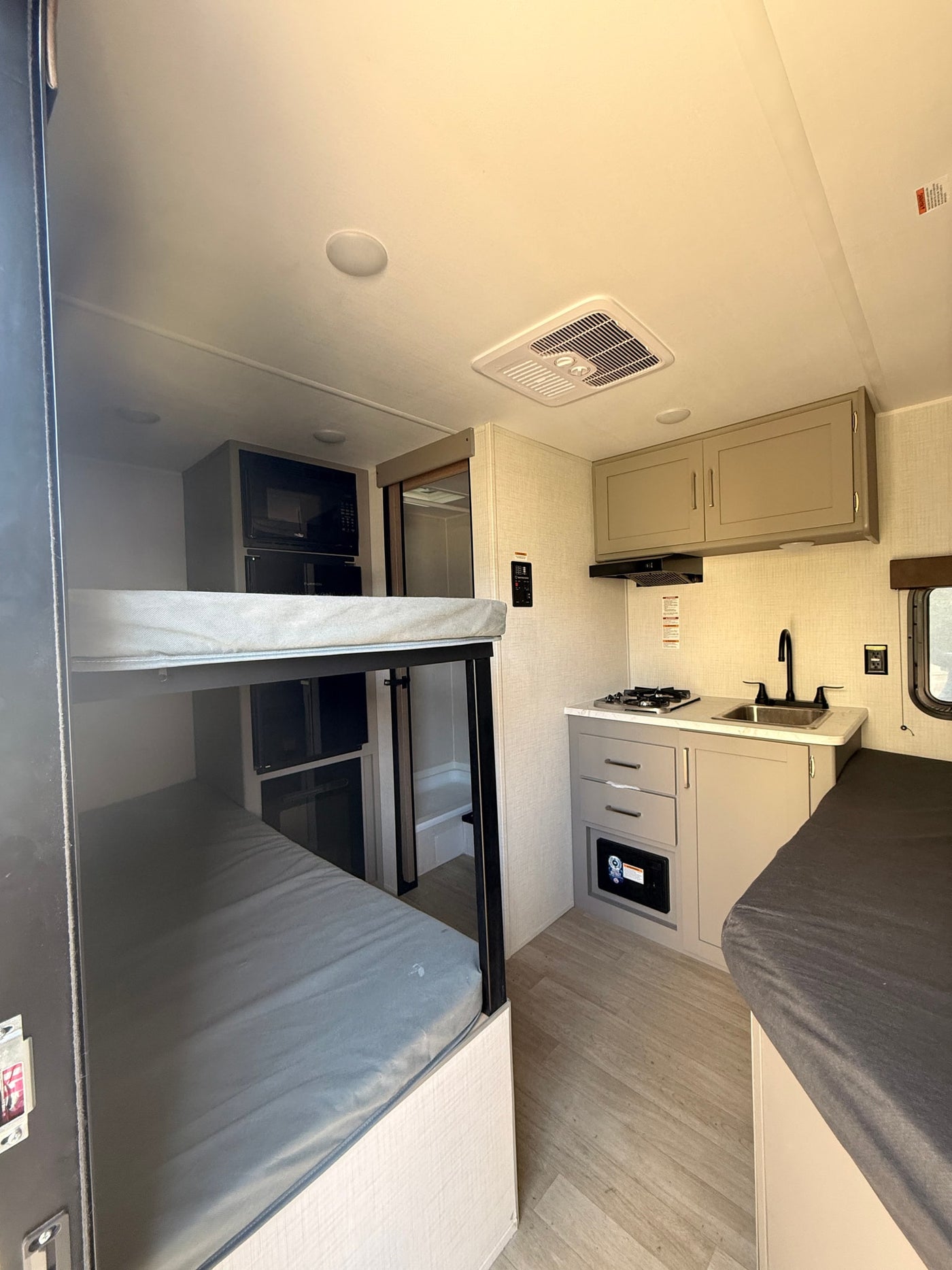Modern RV rental interior showing a compact kitchenette with stove, sink, bunk beds, and a functional shower area. — photo 4