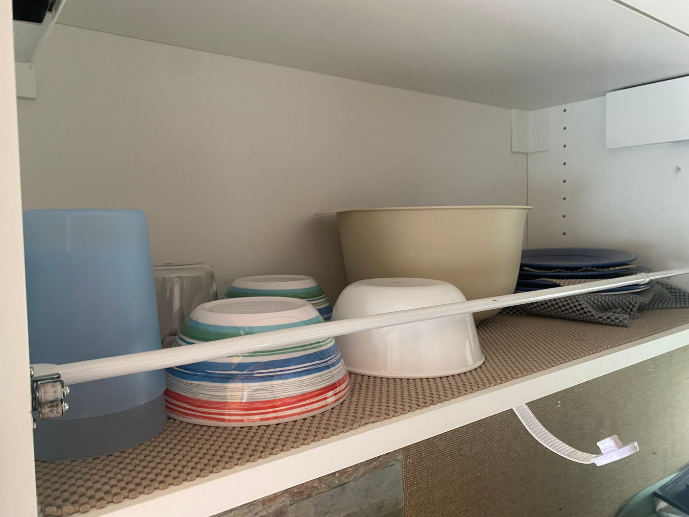 RV rental kitchen cabinet: organized dishes, bowls, cups, plates on a non-slip mat, secured by a tension rod.