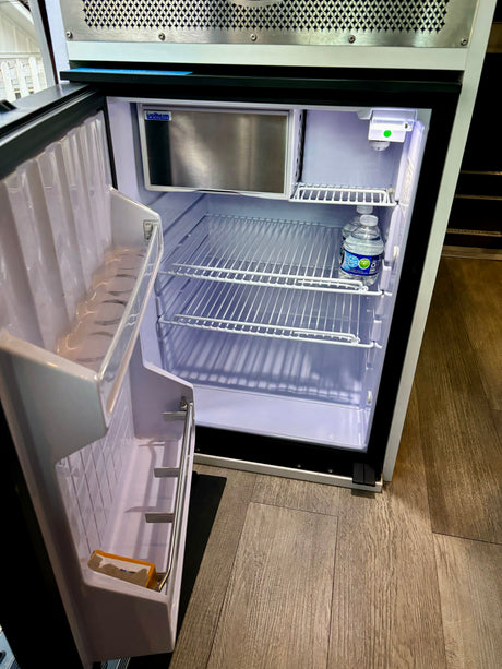 An open mini-refrigerator/freezer in an RV rental, showing wire shelves and two water bottles inside.