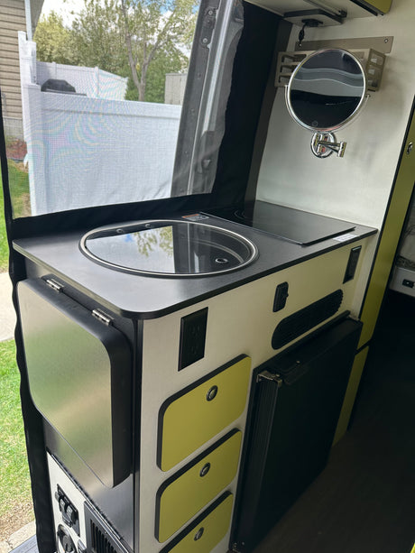 Compact RV rental kitchen area featuring a sink, induction cooktop, fridge, drawers, and a wall-mounted mirror.