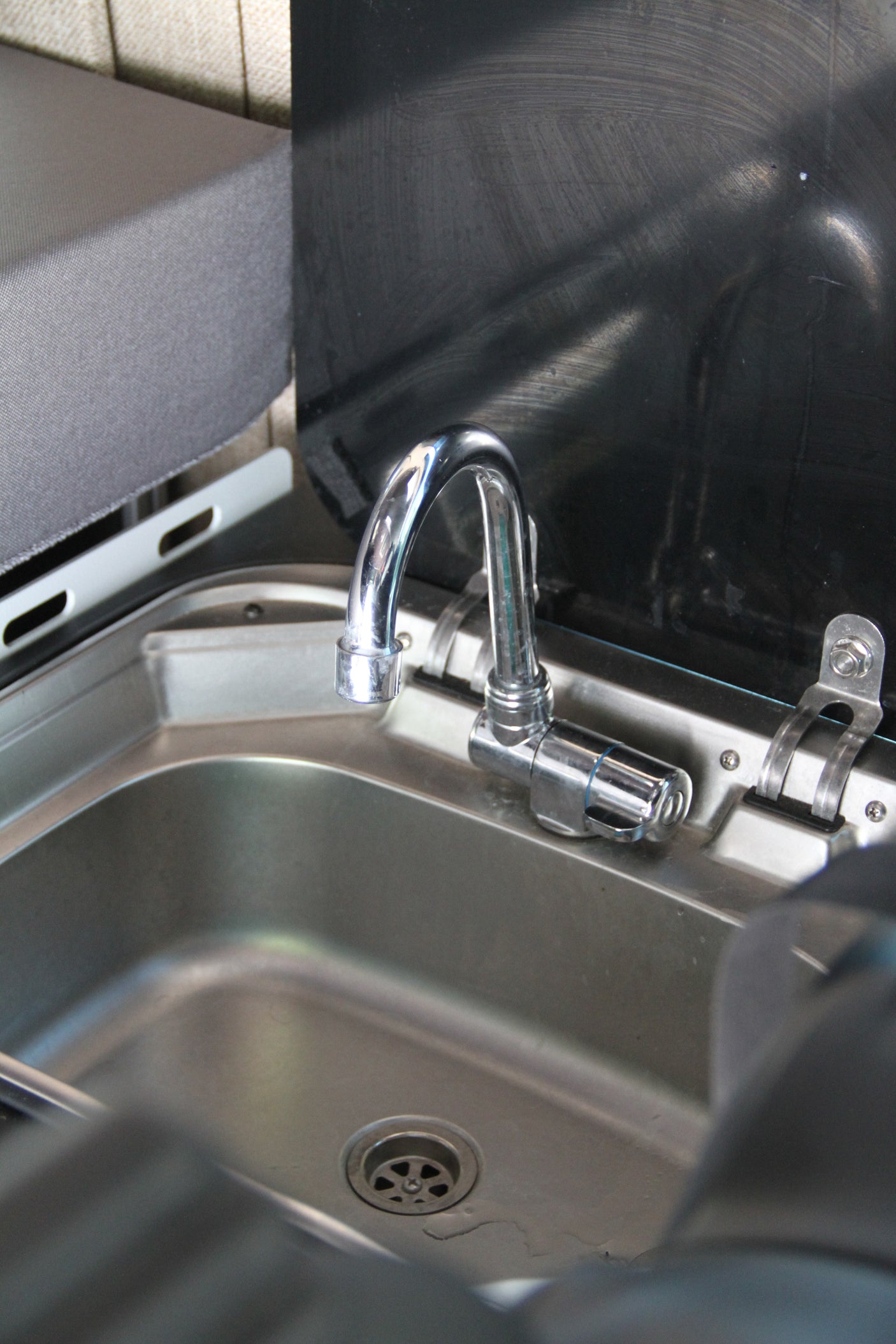 RV rental's compact kitchen area: stainless steel sink, chrome faucet, and black backsplash/cover.