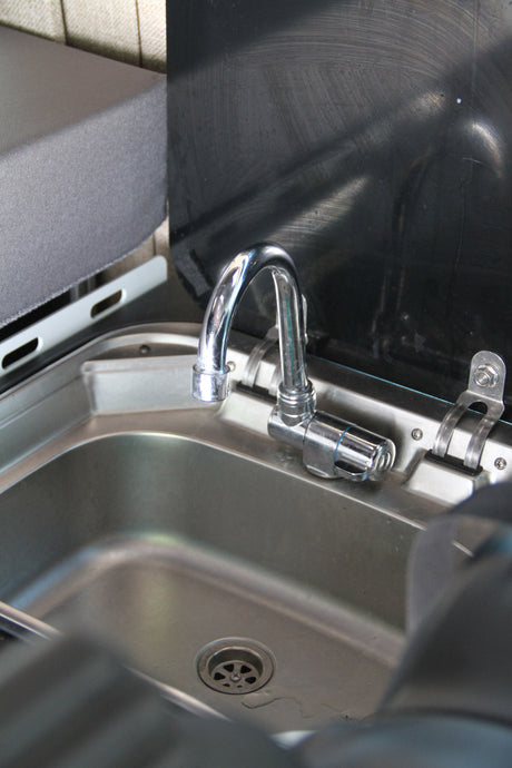 RV rental's compact kitchen area: stainless steel sink, chrome faucet, and black backsplash/cover.