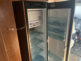 Inside an RV rental: a clean, empty Dometic refrigerator with open doors, showing shelves and bins.