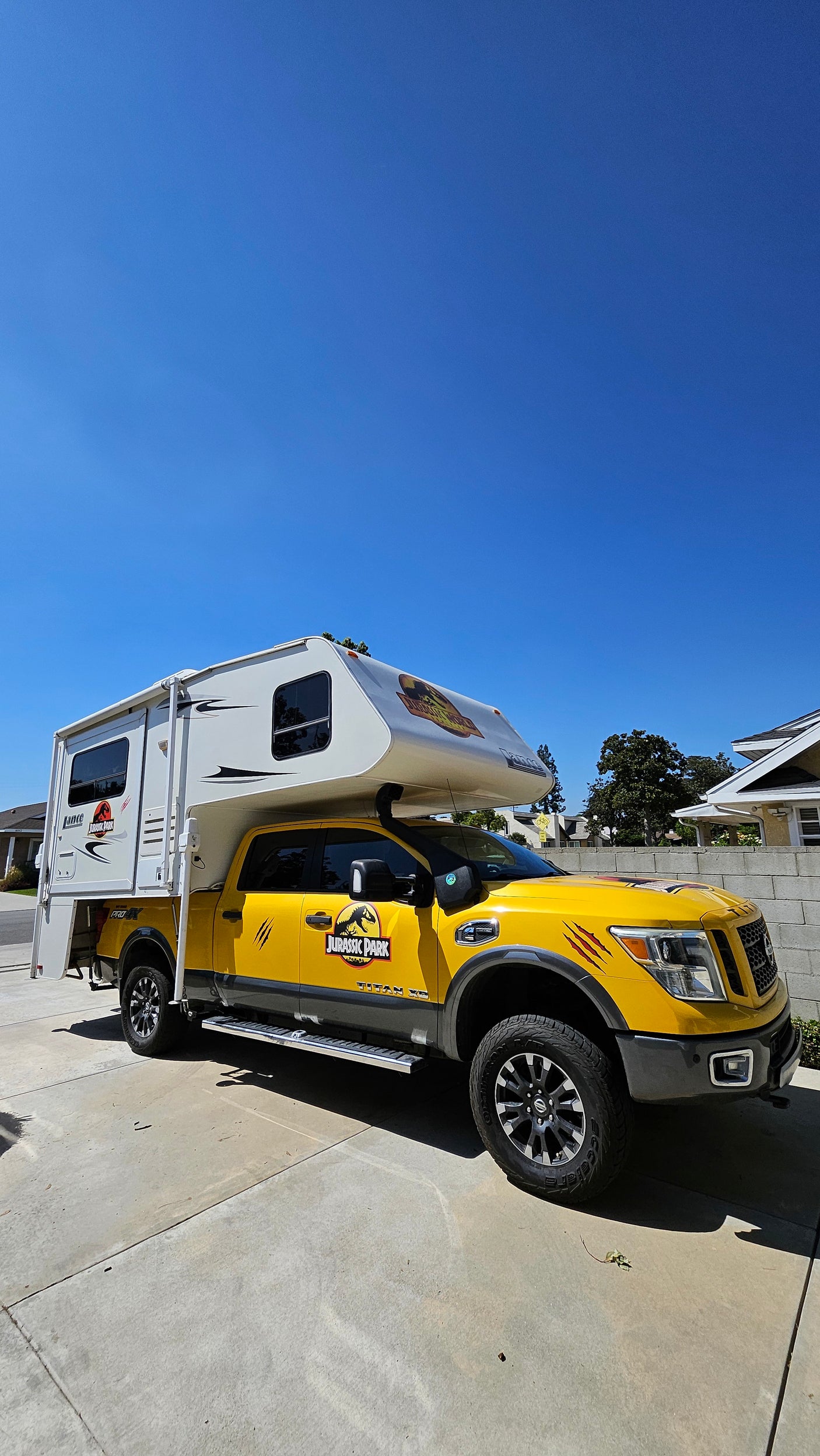 A vibrant yellow Jurassic Park truck with a white camper, perfect as an RV rental for themed adventures.