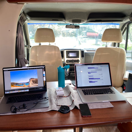 Mobile office setup in an RV rental. Two laptops, water bottle, and accessories on table for remote work and digital nomad lifestyle.