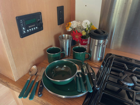 RV rental's equipped kitchen: green enamelware, Stanley mug, stove, and control panel for comfortable camping.