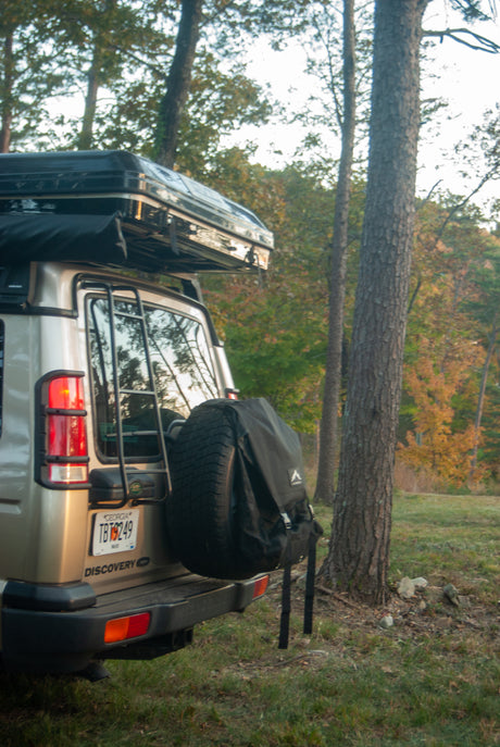 Tan Land Rover Discovery SUV with rooftop tent & rear gear bag, set in a forest, ready for your RV rental journey.