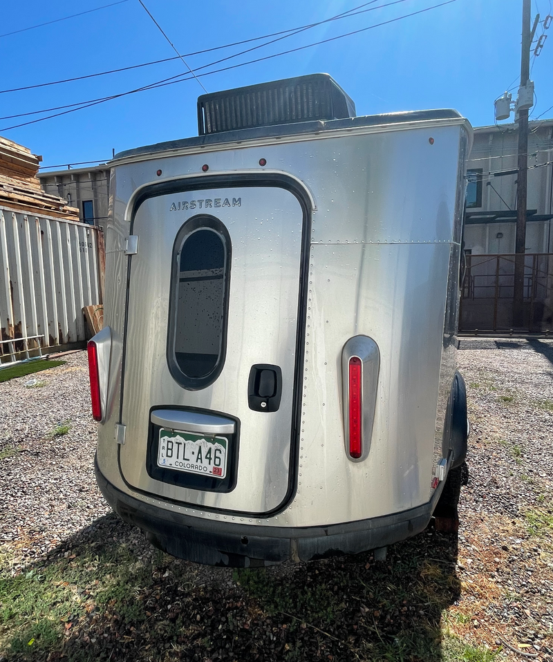 Rear view of a shiny silver Airstream camper with its door, window, and Colorado plate. Ideal for an rv rental, ready for adventure. — photo 3