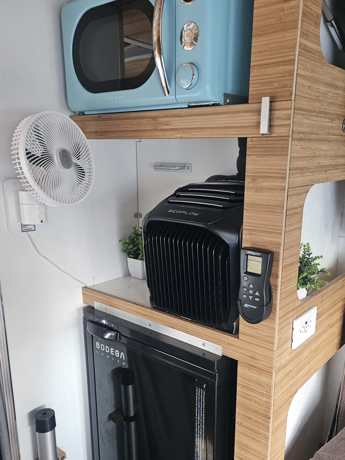 Inside an RV rental: a light blue microwave, portable AC, cooler, fan, and sleek bamboo shelving maximize space. — photo 7