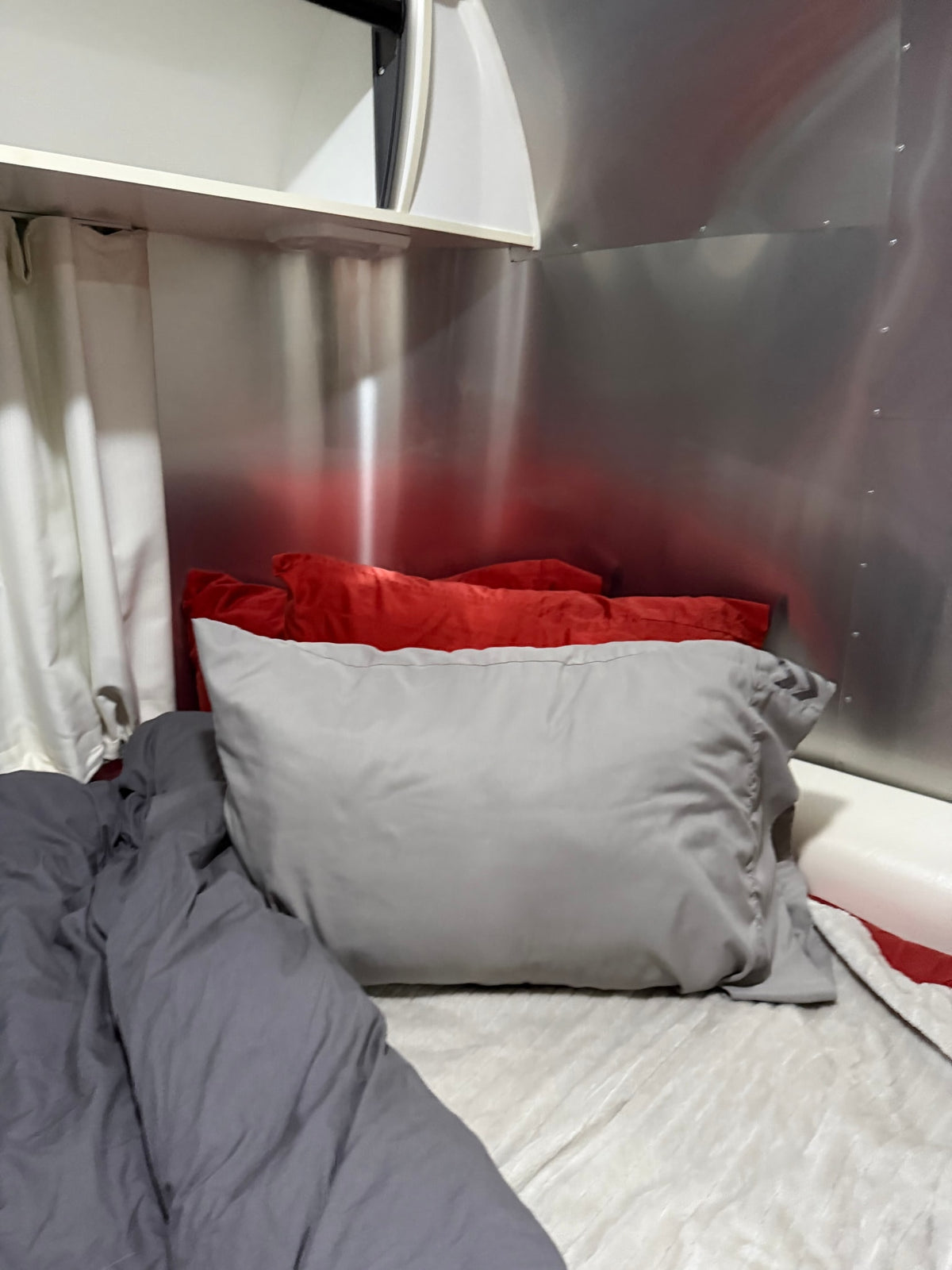 Comfortable RV rental bed with grey duvet, red & grey pillows, set against the metallic interior of an Airstream trailer. — photo 5