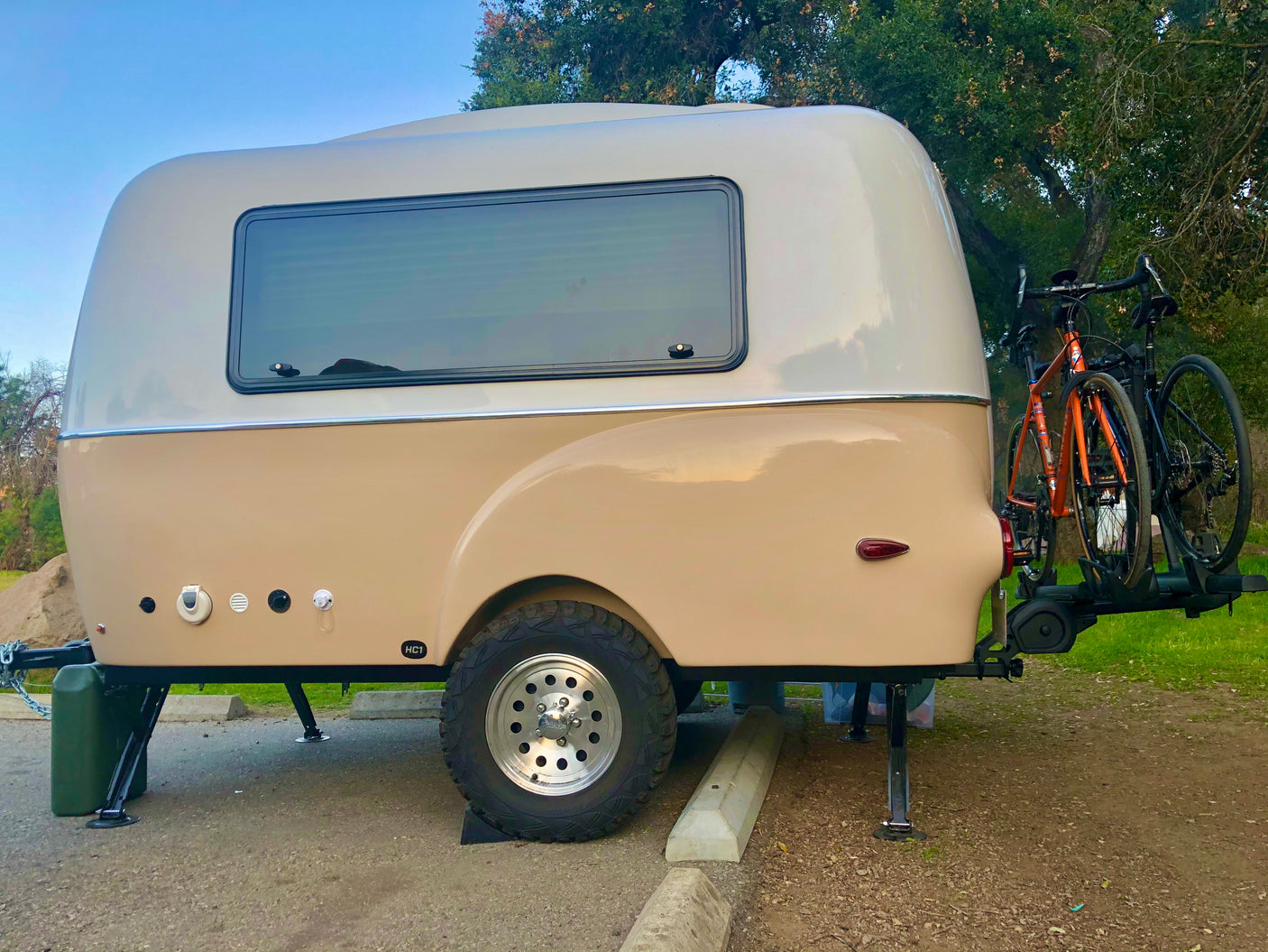 Beige, compact travel trailer with off-road tires and bike rack, perfect for your next RV rental adventure.