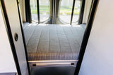 Inside this rv rental, a comfy campervan bed with a patterned mattress and rear windows, ready for your next adventure.