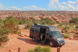 A person reads in an RV rental camper van parked at a scenic red rock canyon campsite, offering stunning desert views.