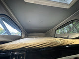 Cozy pop-top RV rental sleeping area with open windows showing trees, a comfortable fluffy bed, and convenient USB charging ports.