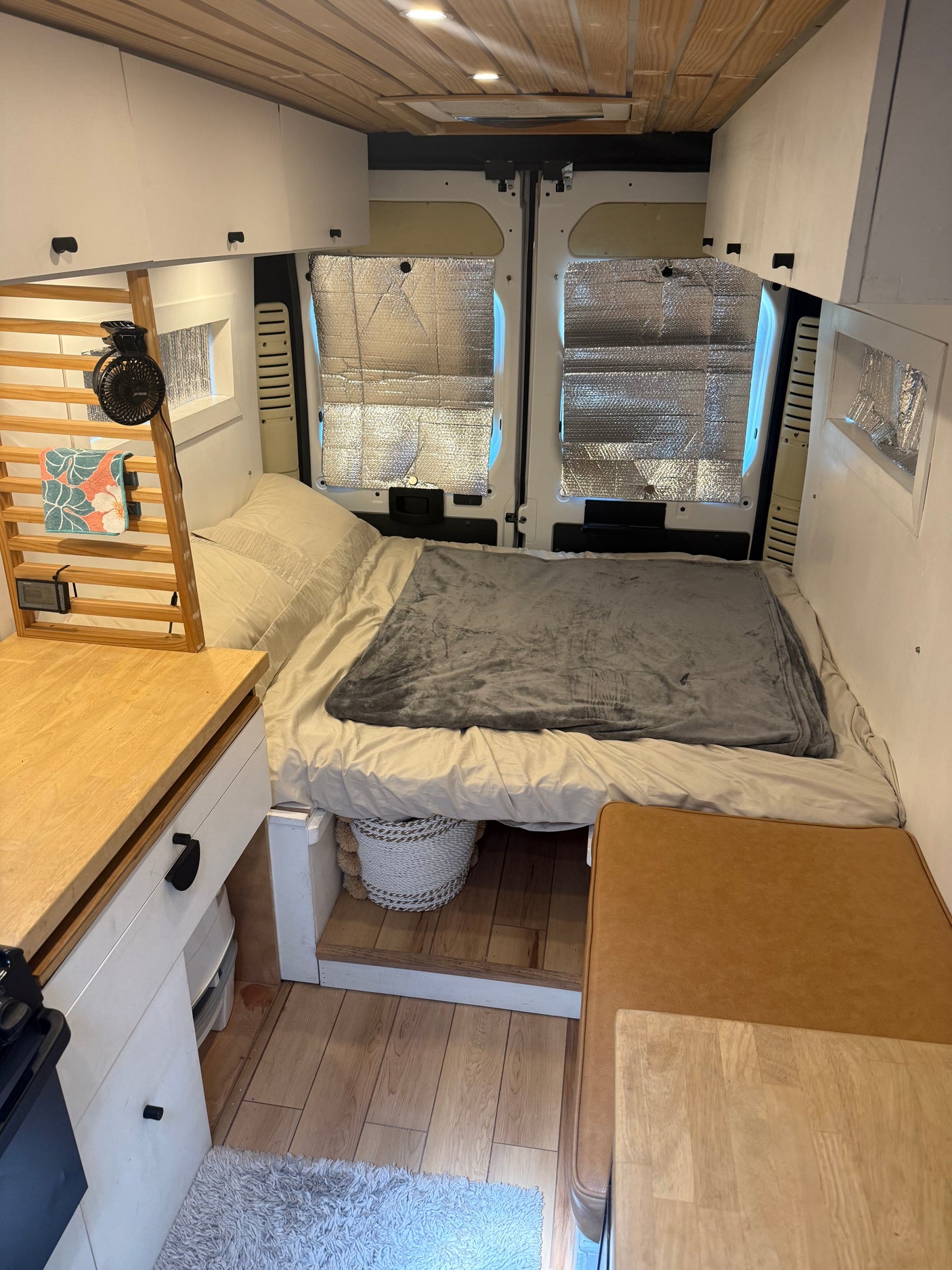 Inside a cozy rv rental camper van: bed at rear, compact kitchen on left, overhead cabinets, and wood ceiling.