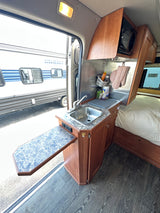 Inside this RV rental: kitchen with sink, microwave, and expandable counter. Adjacent cozy sleeping area for comfort.
