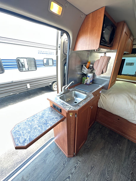 Inside this RV rental: kitchen with sink, microwave, and expandable counter. Adjacent cozy sleeping area for comfort.