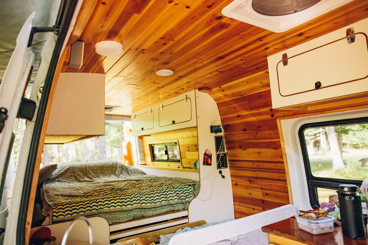 Warm, wood-paneled RV rental interior with a comfy bed, overhead cabinets, and counter space.