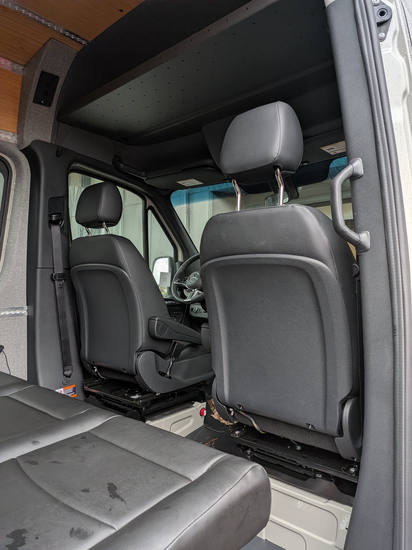 View inside an RV rental: front driver/passenger seats, steering wheel, and custom ceiling with wood and fabric paneling.