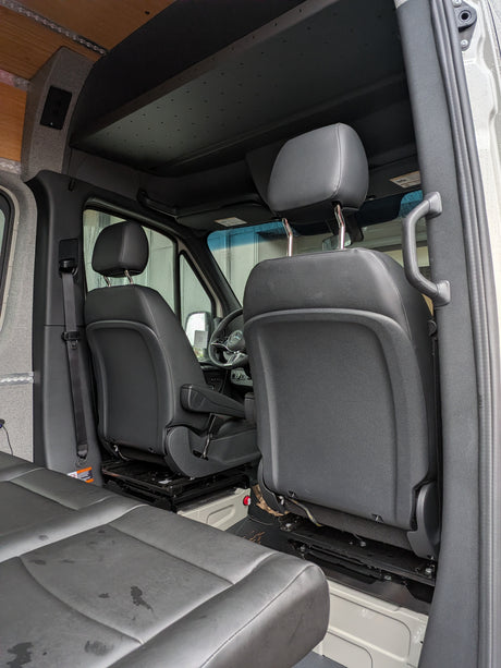 View inside an RV rental: front driver/passenger seats, steering wheel, and custom ceiling with wood and fabric paneling.