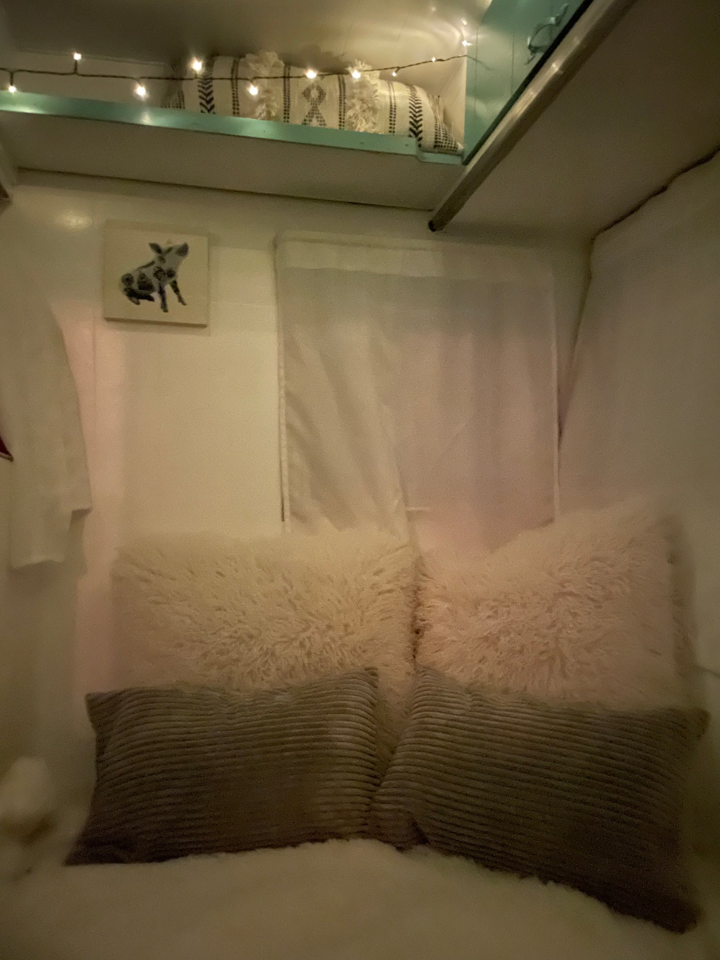 Relax in this cozy RV rental interior, featuring a comfortable bed with plush pillows, string lights, and charming pig art. — photo 12