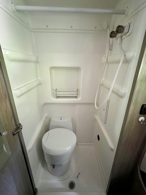 Compact RV rental wet bath featuring a toilet, shower, and showerhead for convenient travel.