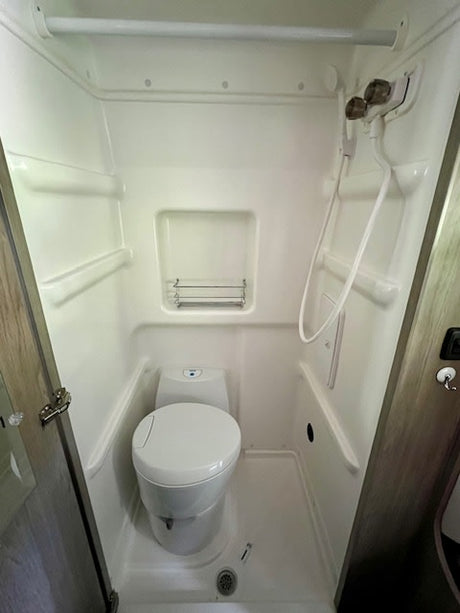 Compact RV rental wet bath featuring a toilet, shower, and showerhead for convenient travel.