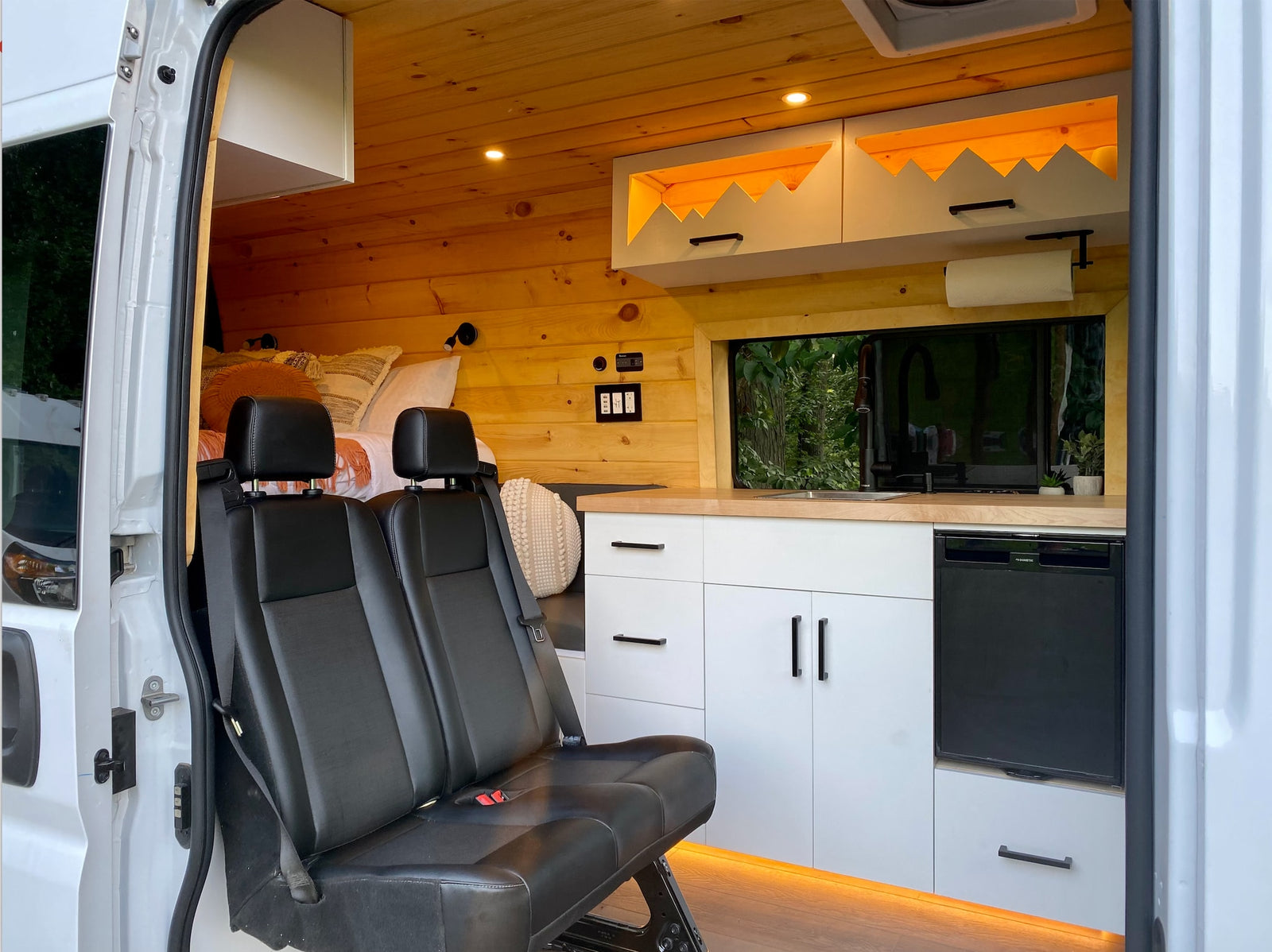 This cozy rv rental interior features a functional kitchen, comfortable bed, and passenger seating, ideal for road trips.