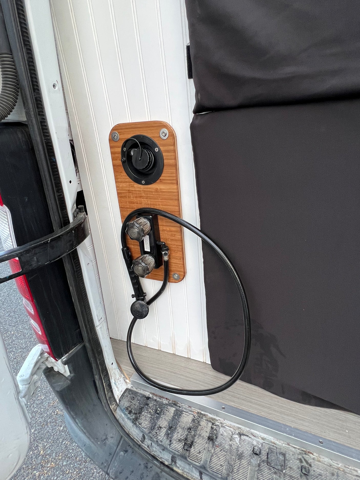 RV rental: Rear area features an outdoor shower station with controls, hose, and water fill on a wood panel.