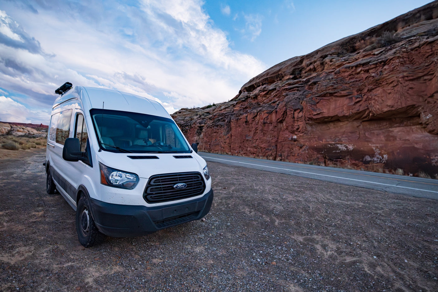 White Ford Transit camper van RV rental parked by a red rock canyon. Perfect for your next desert road trip adventure.